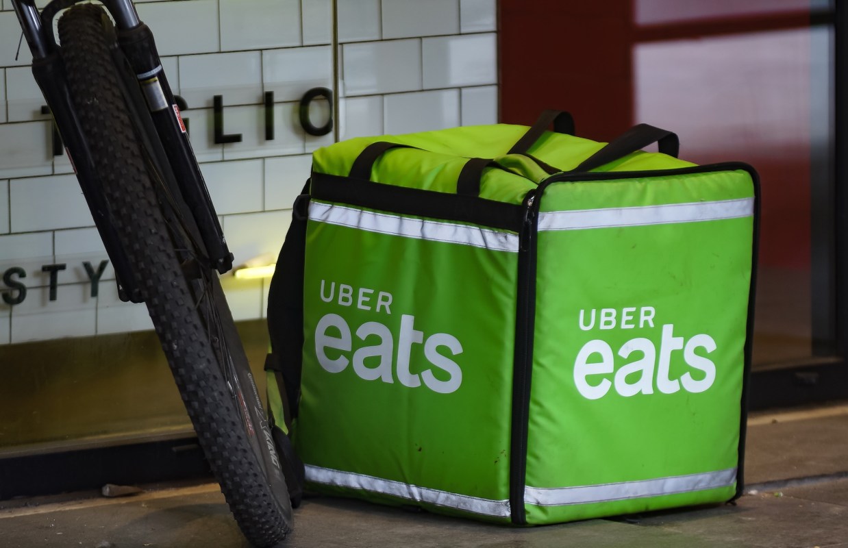 A green Uber Eats delivery bag is placed next to a bicycle near a restaurant entrance.