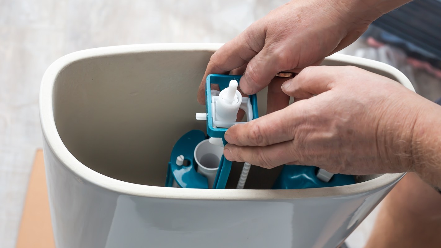 A person installs parts inside a toilet tank.