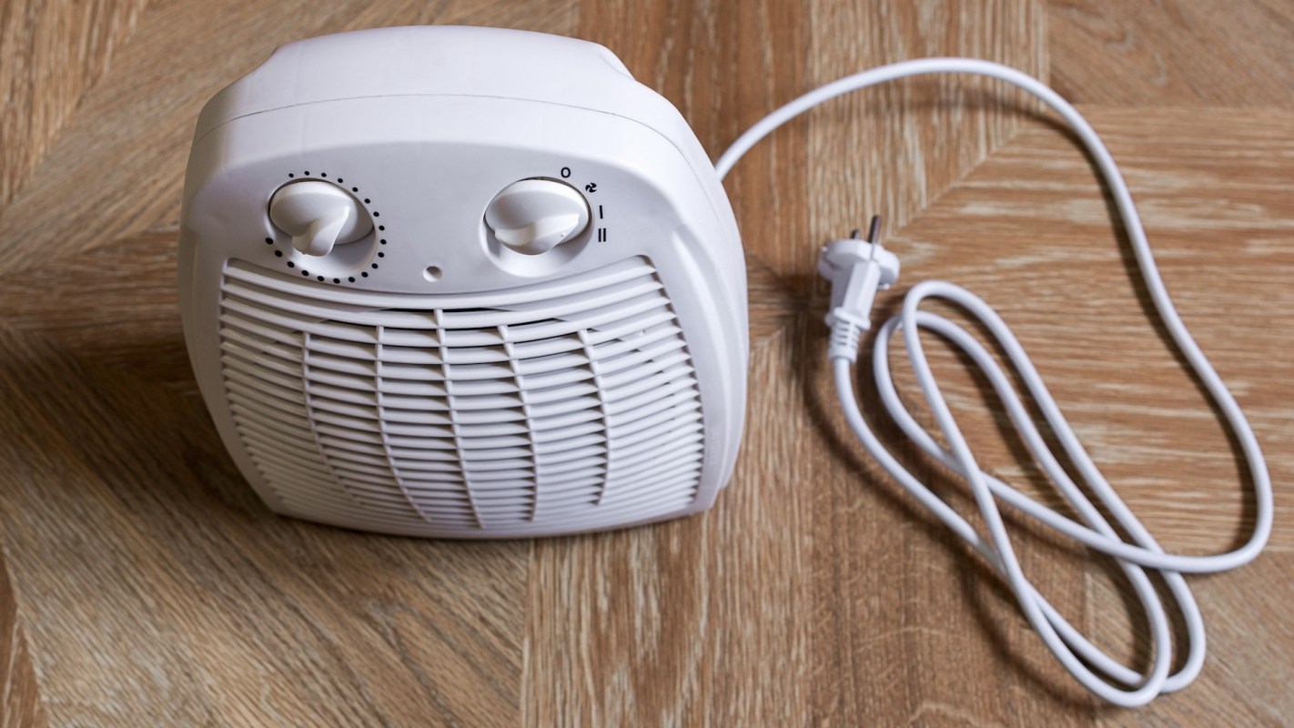 A white electric space heater with a power cord on a wooden floor.