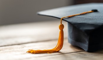 A graduation cap with an orange tassel on a wooden surface.
