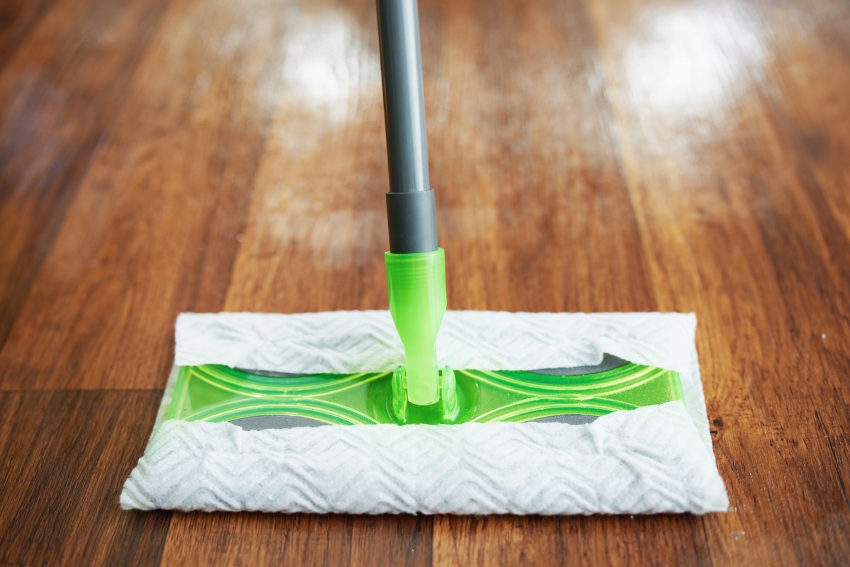 A mop with a green cleaning pad positioned on wooden flooring.