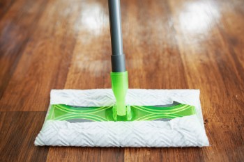 A mop with a green cleaning pad positioned on wooden flooring.