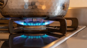 A pot on a gas stove with a blue flame underneath.