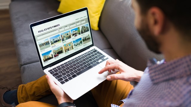A person browsing a real estate website on a laptop while sitting on a couch.