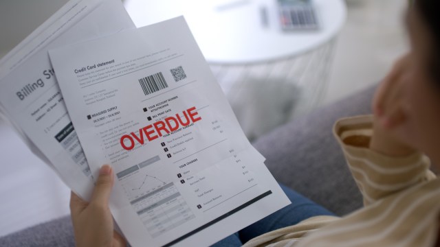 A person holding a stack of bills, including a credit card statement marked "OVERDUE."