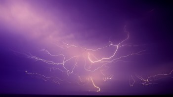 A dramatic display of lightning in a purple sky over the water.