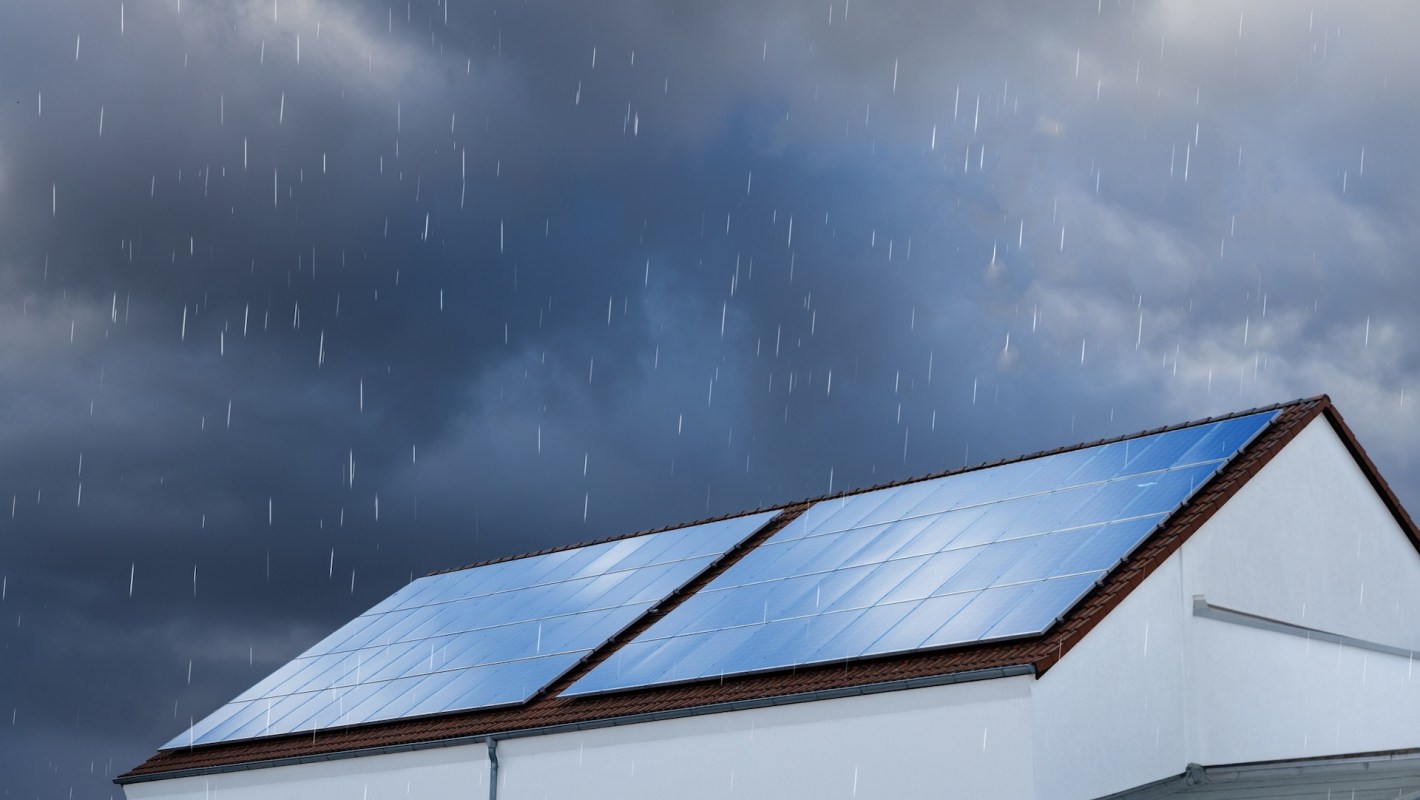 A house with solar panels on the roof under a rainy and cloudy sky.