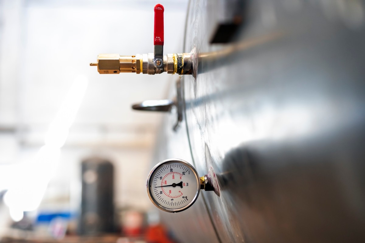 A pressure gauge and valve on a large metal tank in an industrial setting.