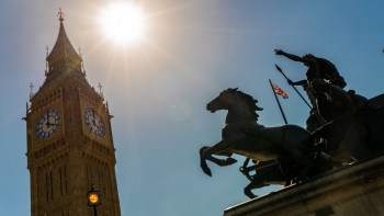 The sun shines brightly over Big Ben and a Union Jack flag flying behind the famous Boadicea statue in London.