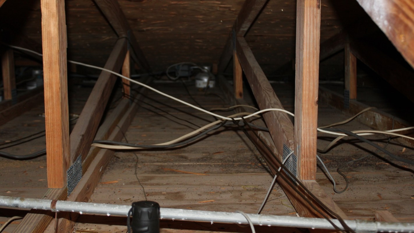 An interior view of an attic with wooden beams and exposed electrical wiring.