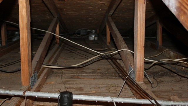 An interior view of an attic with wooden beams and exposed electrical wiring.