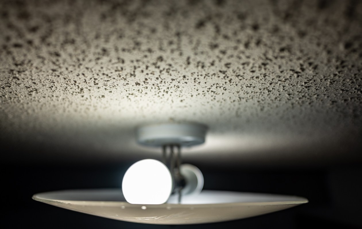 A ceiling light fixture with a glowing bulb on a popcorn ceiling.