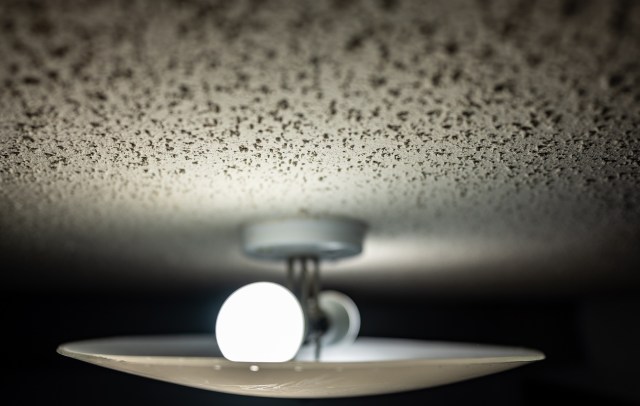 A ceiling light fixture with a glowing bulb on a popcorn ceiling.