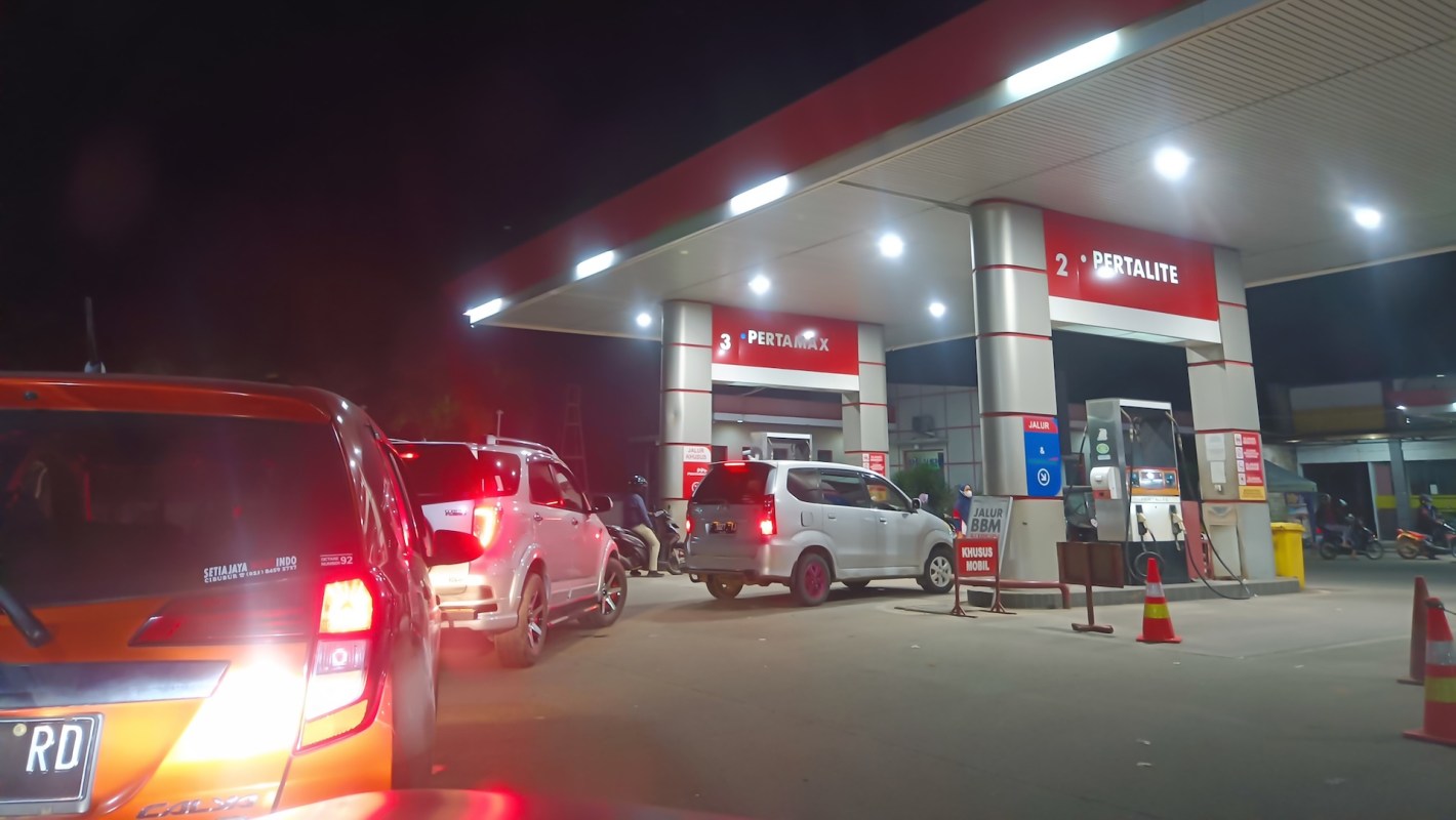 Cars queueing at a gas station at night.