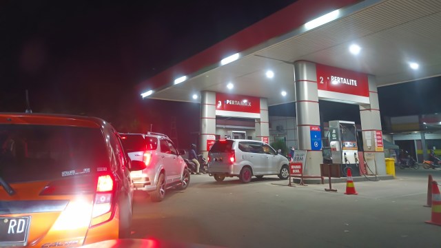 Cars queueing at a gas station at night.