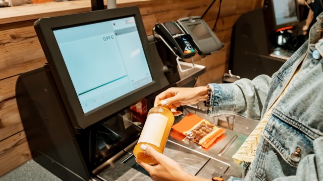 A person scans a bottle of beverage at a self-checkout kiosk.