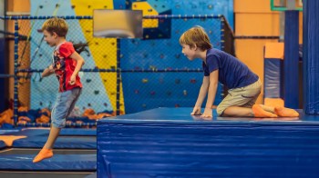 Two boys with orange socks are playing on a blue foam platform in a trampoline park.
