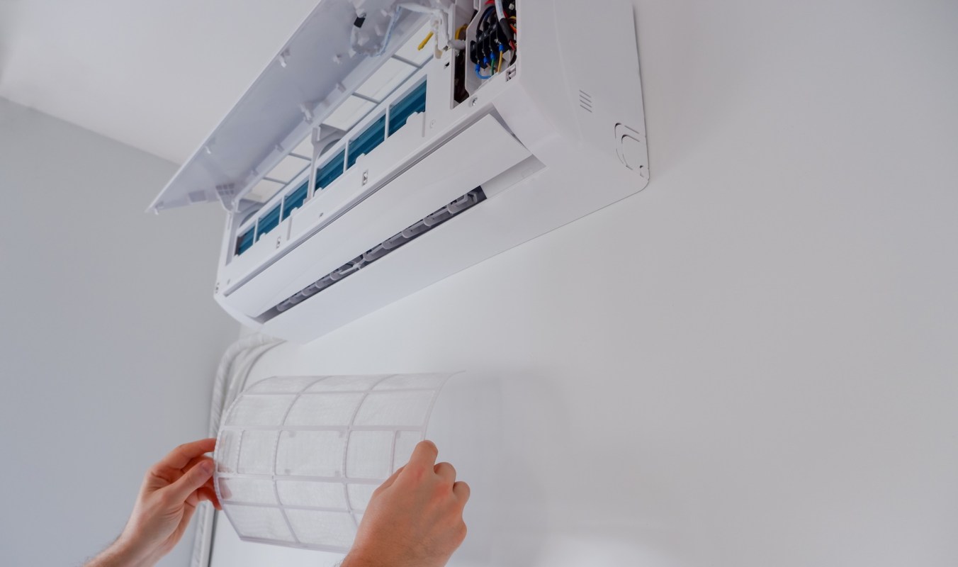 A person removes a filter from a mini-split unit mounted on a wall.