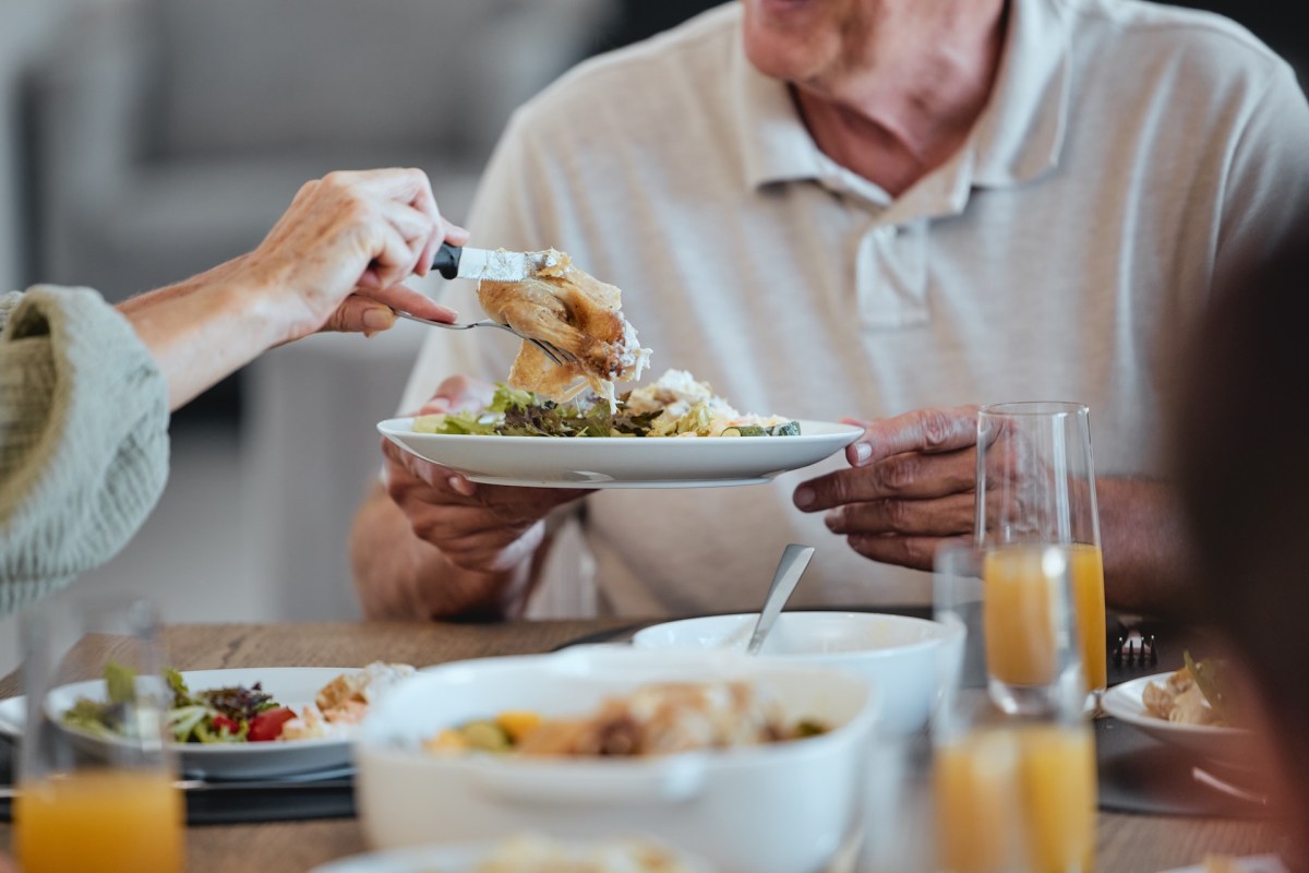 A person serves food onto a plate during a meal at a dining table.