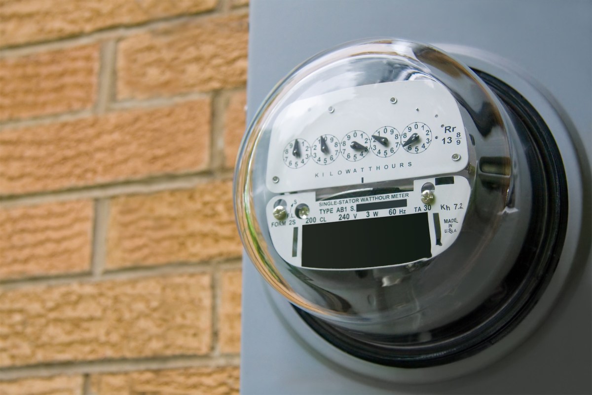 An electric meter mounted on a wall with a brick background.