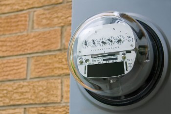 An electric meter mounted on a wall with a brick background.