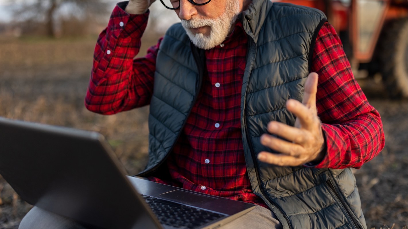 A farmer in distress in front of his laptop.