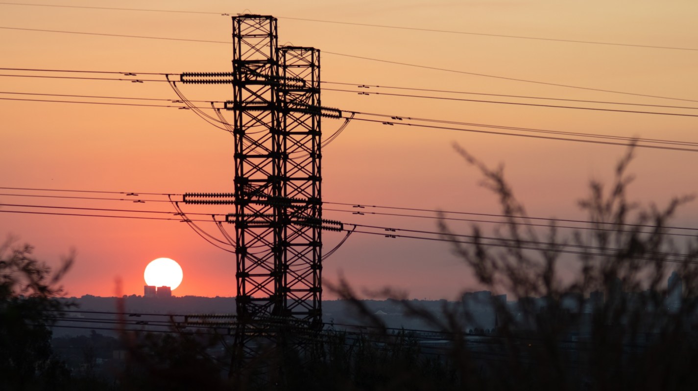 A power line tower silhouetted against a sunset with orange and pink hues.