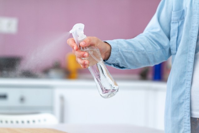 A hand sprays liquid from a clear spray bottle in a kitchen setting.