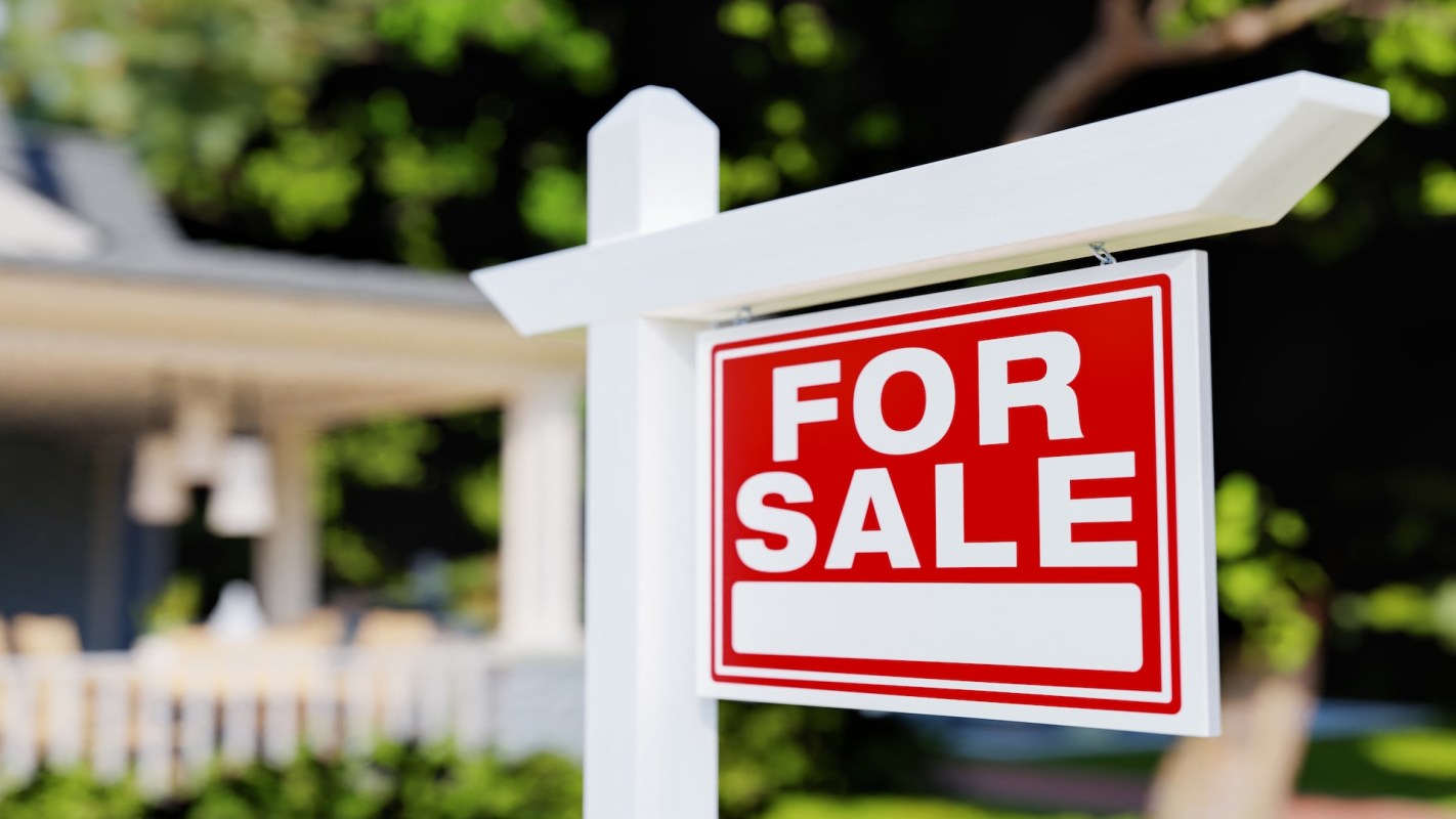 A "For Sale" sign posted in front of a house with a blurred background.
