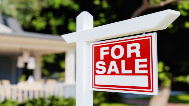 A "For Sale" sign posted in front of a house with a blurred background.