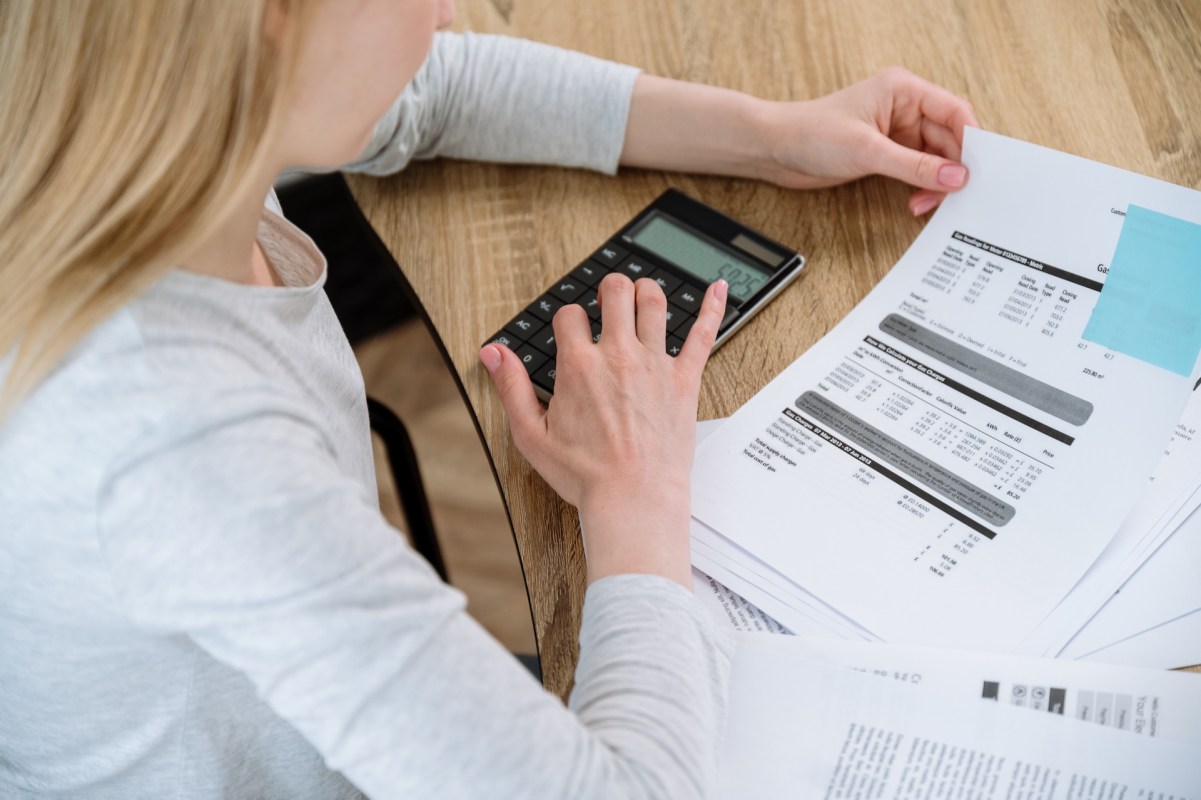 A person using a calculator while reviewing printed documents on a wooden table.