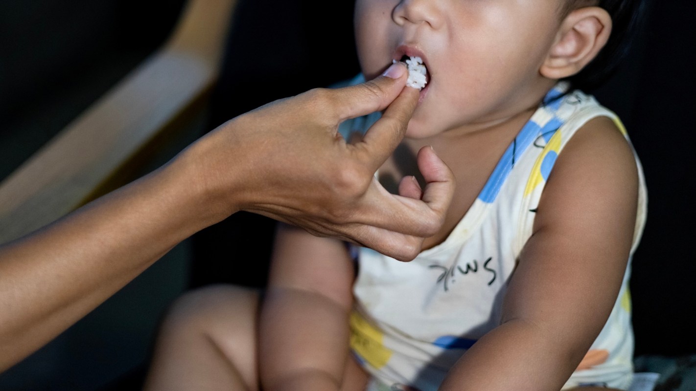 A hand feeds a small child a piece of food.