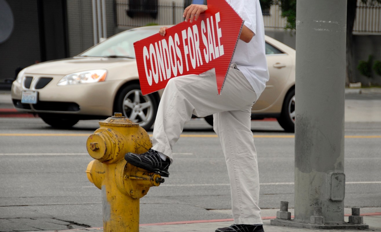 A person stands on a fire hydrant holding a sign that reads "Condos for Sale."