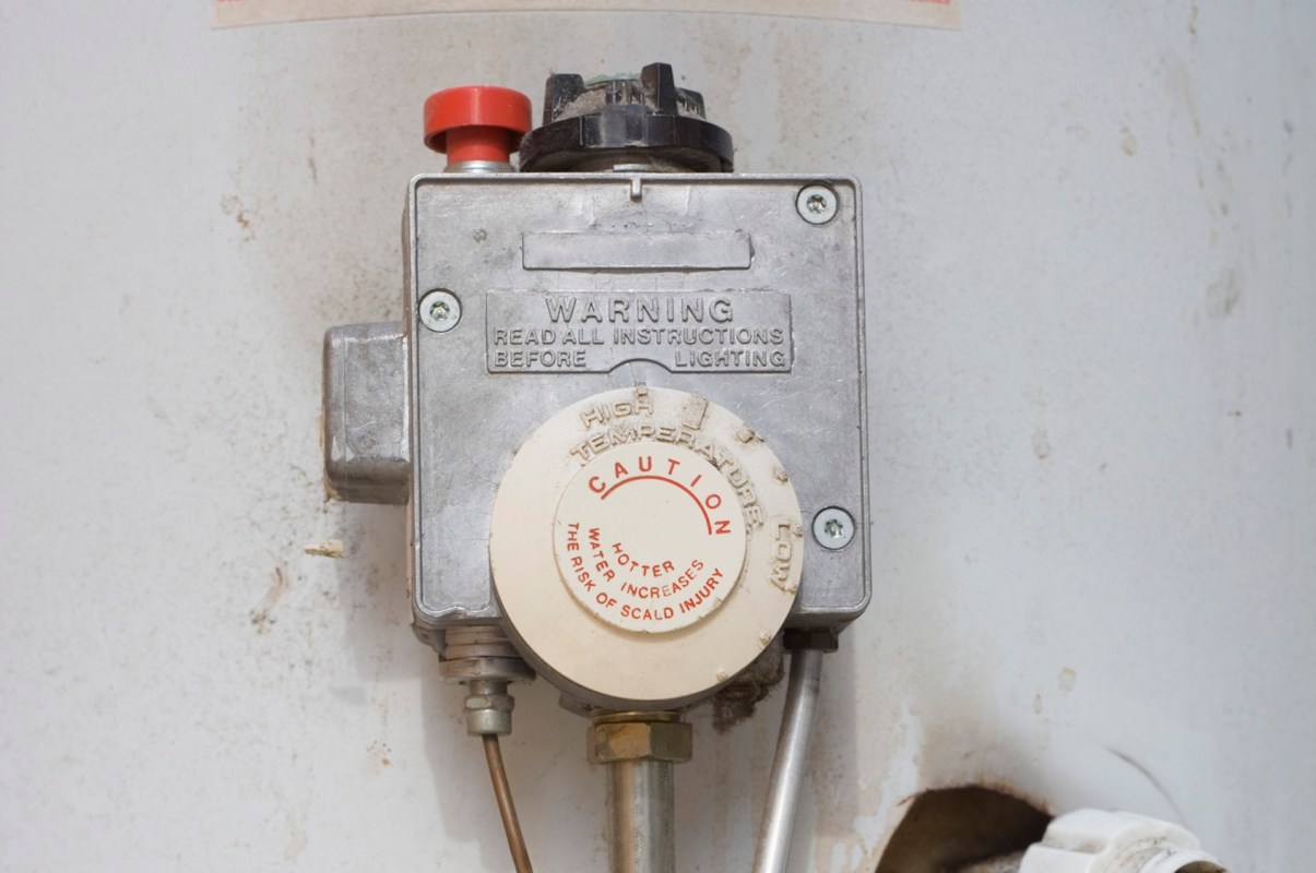 A gas valve with a warning label and temperature adjustment dial mounted on a wall.