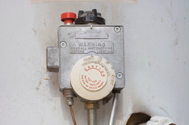 A gas valve with a warning label and temperature adjustment dial mounted on a wall.