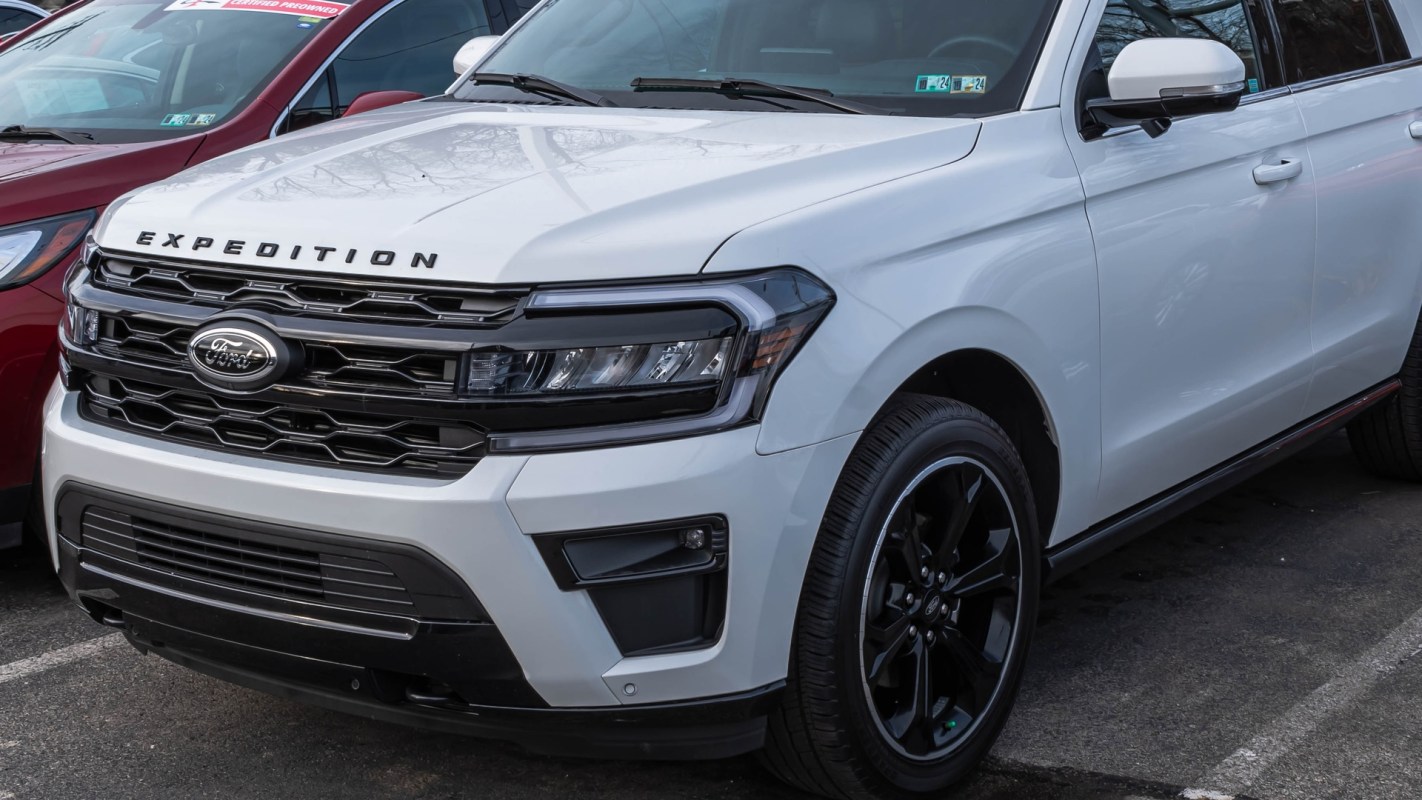 A white Ford Expedition parked next to a red vehicle in a parking lot.