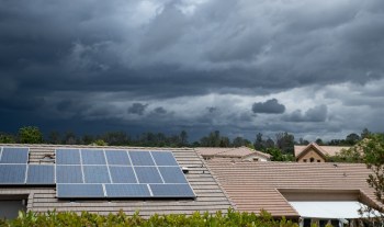 Solar panels on rooftops with dark storm clouds in the background.