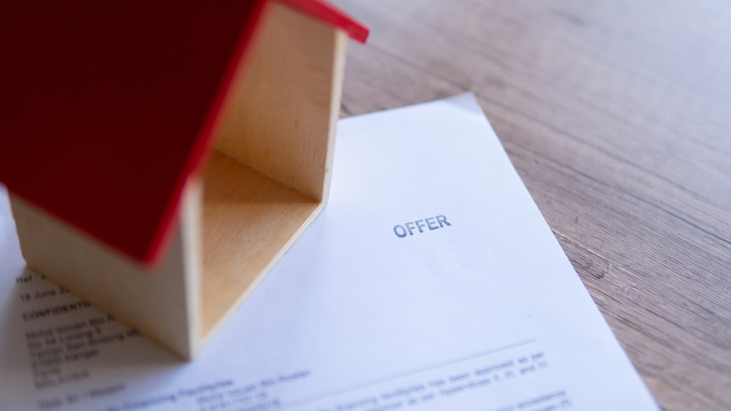 A small wooden house model is placed on top of an offer letter.