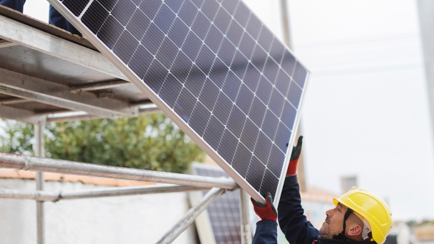 A worker installs a solar panel while on a scaffold.