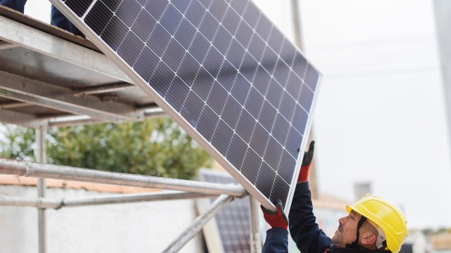 A worker installs a solar panel while on a scaffold.