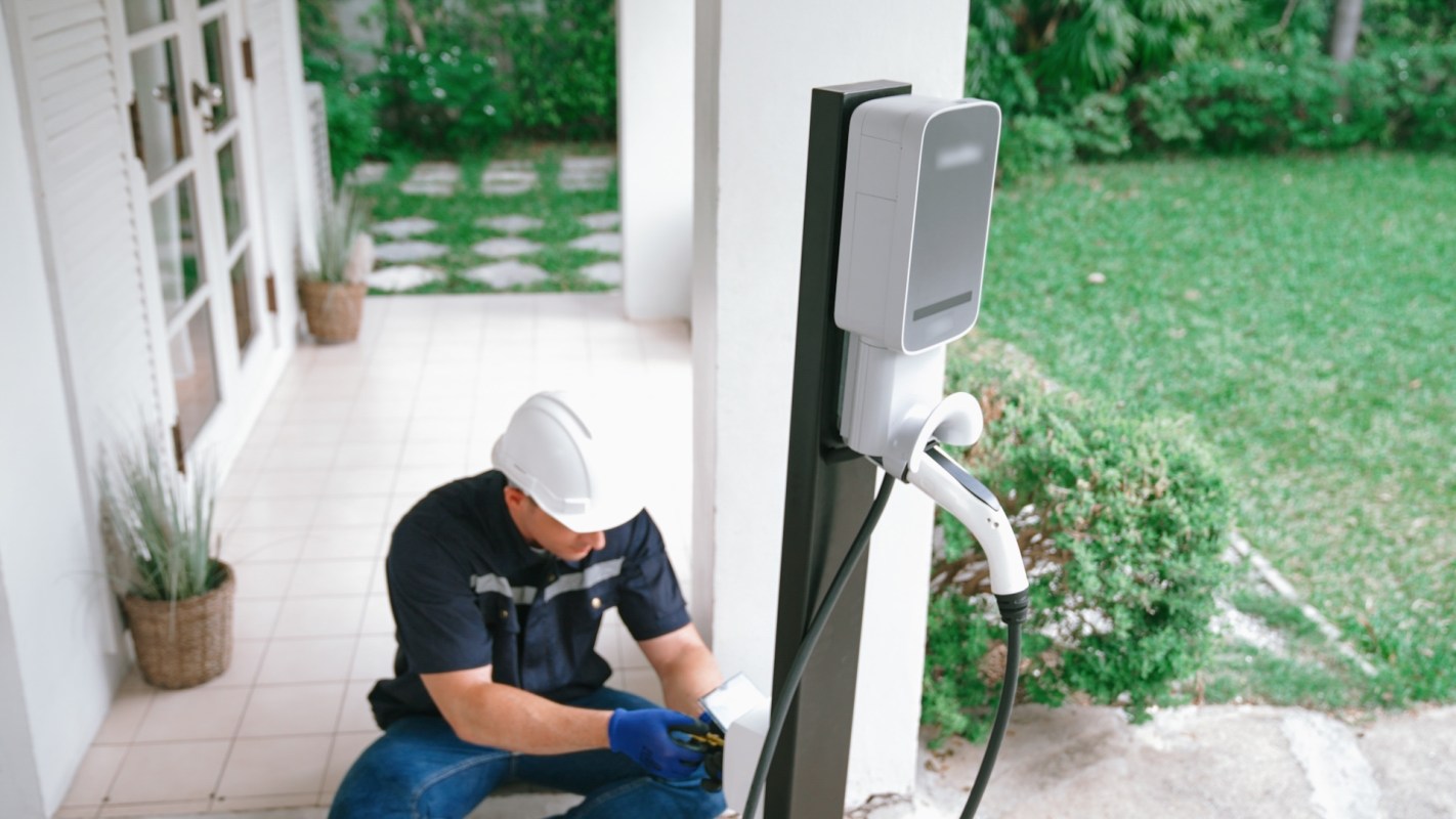 A technician installs an electric vehicle charging station outside a house.