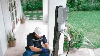 A technician installs an electric vehicle charging station outside a house.