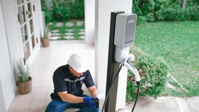 A technician installs an electric vehicle charging station outside a house.