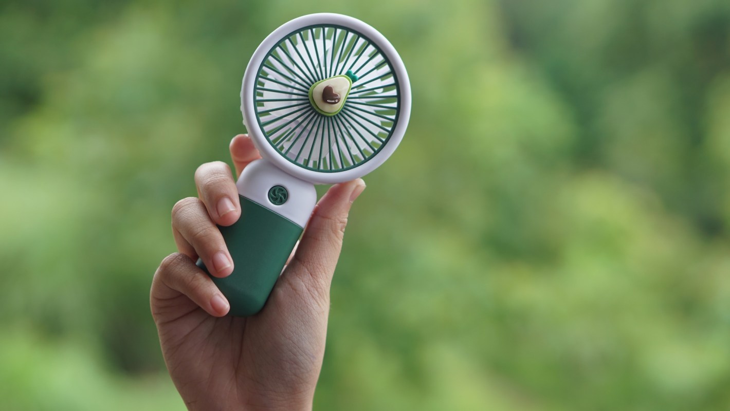 A person holding a handheld portable fan against a blurred green background.