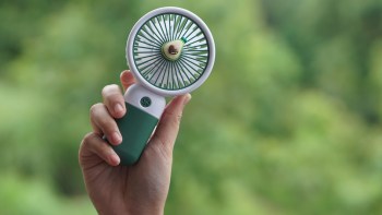A person holding a handheld portable fan against a blurred green background.