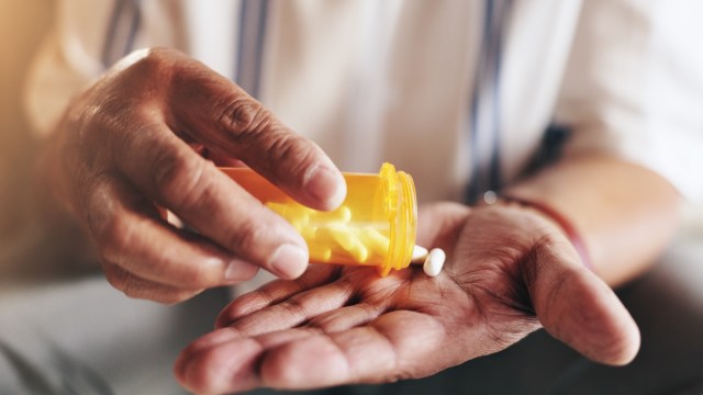 A person pours pills from an orange prescription bottle into their hand.
