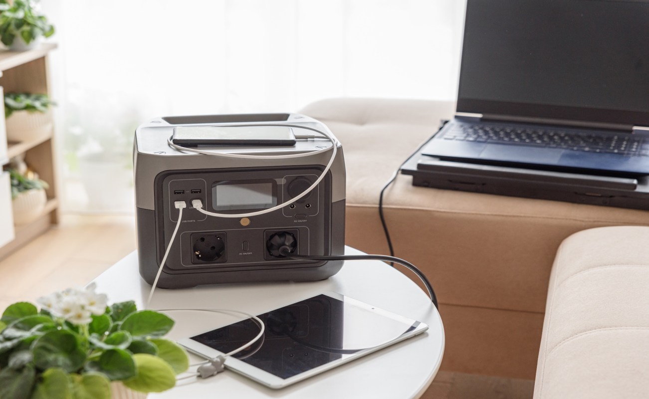 A portable power station connected to a tablet and a laptop on a coffee table.