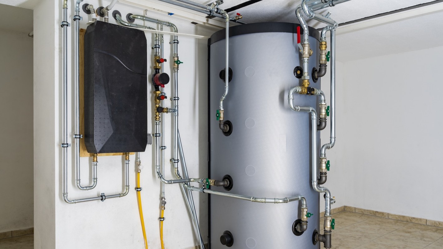 Pipes and a large tank are mounted on a wall in a mechanical space.