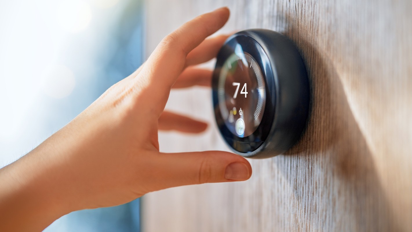 A hand adjusts a digital thermostat displaying a temperature of 74 degrees.