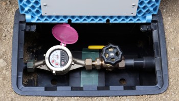 A water meter and valve housed in a plastic box with a pink cover lid.